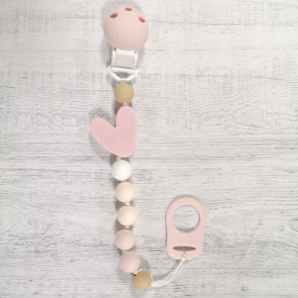 pink heart silicone pacifier clip and adapter on wood surface
